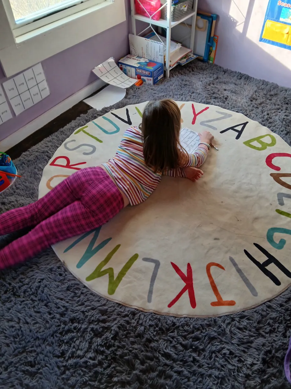 Child lying on an alphabet rug working through a reading worksheet