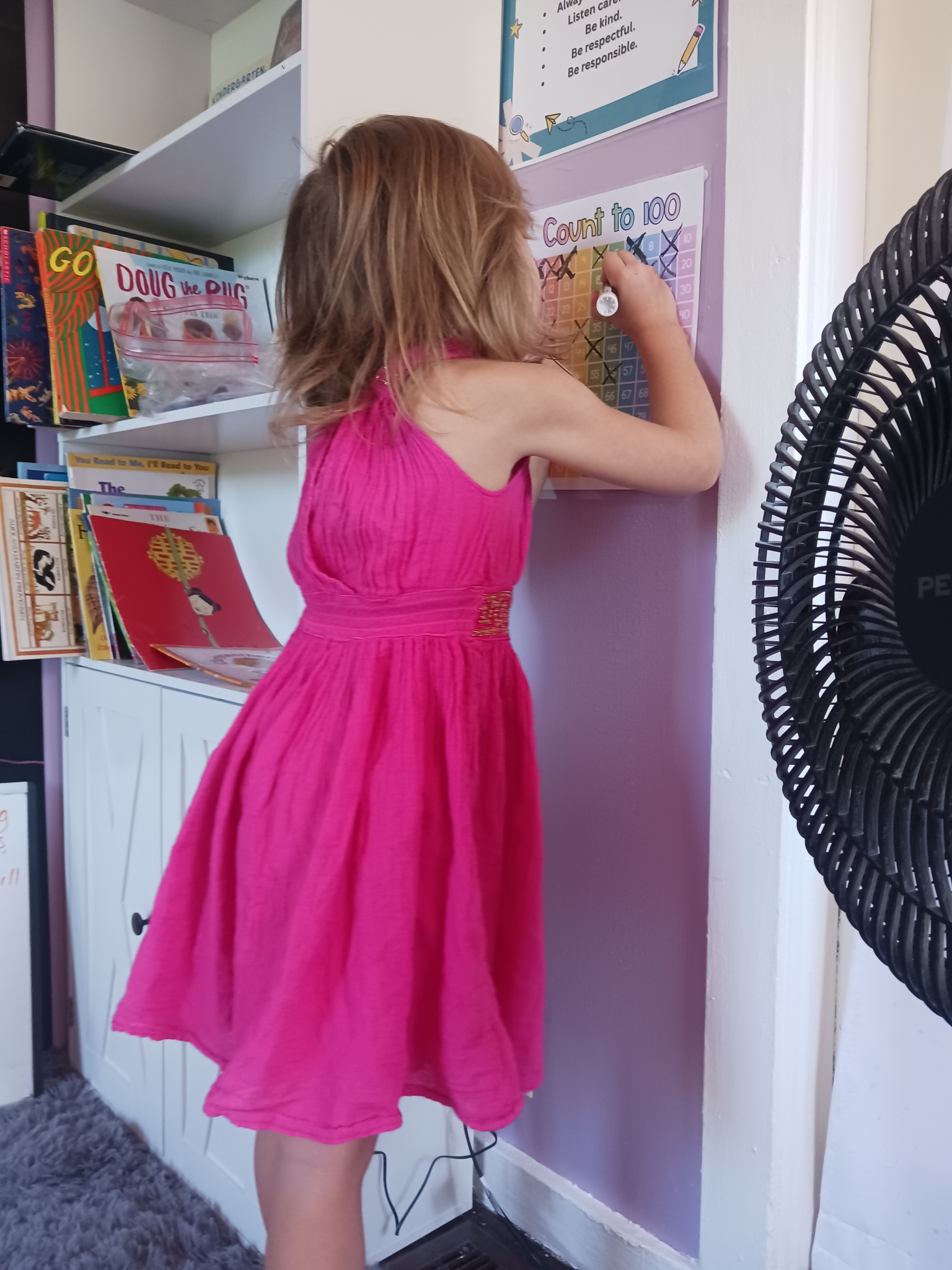 Child marking a Count to 100 chart on the wall